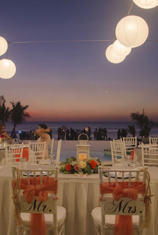 An outdoor wedding reception setup near a beach at sunset with decorated tables, chairs labeled 