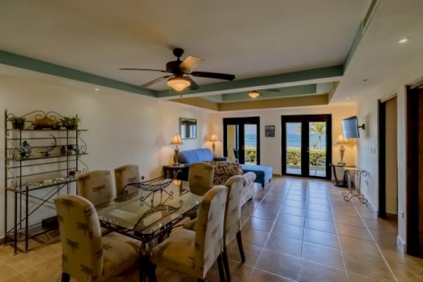 A cozy living and dining area with tiled flooring, ceiling fan, and patio doors leading outside. Decorated with cushioned chairs and elegant lighting.