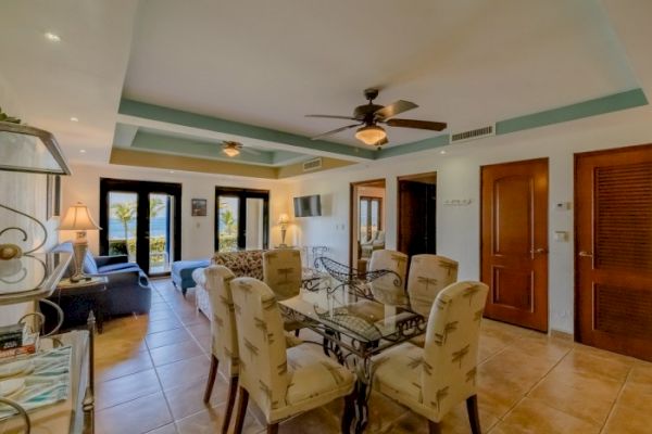 A well-furnished living area with a dining table, chairs, ceiling fans, and doors leading to a balcony or patio with a view of the outdoors.