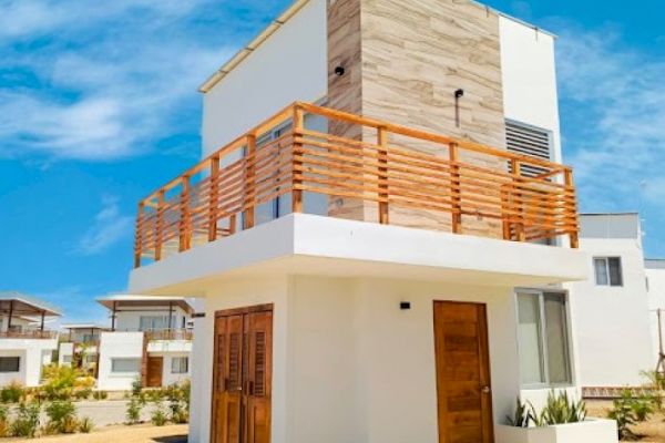 This image shows a modern two-story house with wooden railings and doors, featuring a combination of white and natural wood exterior elements under a clear sky.