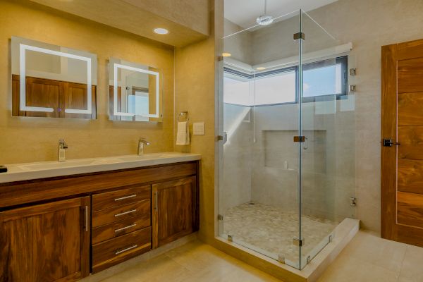 The image shows a modern bathroom with a wooden vanity, two illuminated mirrors, and a glass-enclosed shower area with a window.