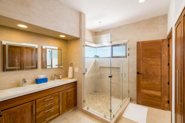 This image shows a modern bathroom with a double vanity, wooden cabinets, and a glass-enclosed shower area.