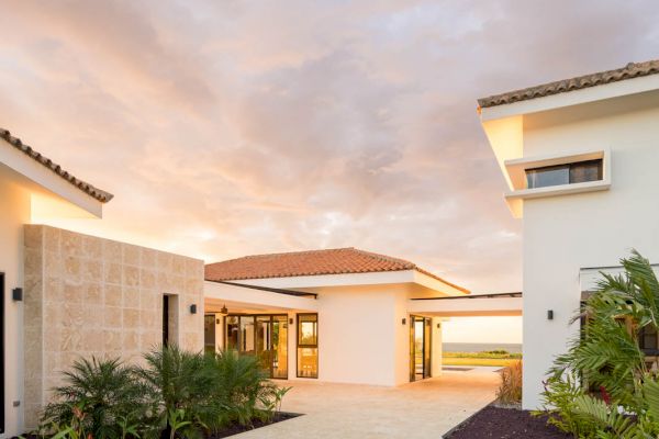 A modern house with white walls and a tile roof, featuring a landscaped entrance path and lush greenery, under a stunning cloudy sky.