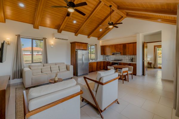 This image shows a modern open-concept living area with a kitchen, dining space, and seating area, featuring wooden ceilings and neutral-toned furniture.