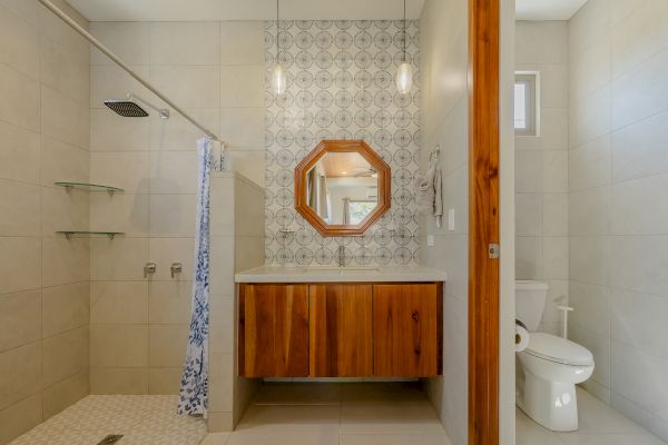 A modern bathroom with a walk-in shower, a wood-accented vanity with a round mirror, and a toilet on the right side of the room.