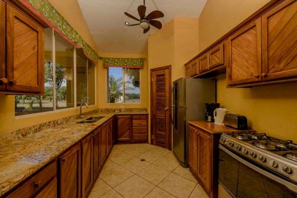 A kitchen featuring wooden cabinets, granite countertops, a refrigerator, a stove, a kettle, a toaster, a ceiling fan, and windows with a scenic view.