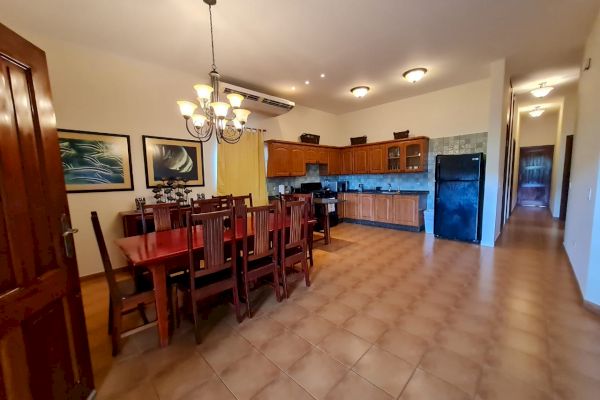 A spacious kitchen and dining area featuring wooden furniture, a chandelier, wall art, and appliances such as a refrigerator and stove.