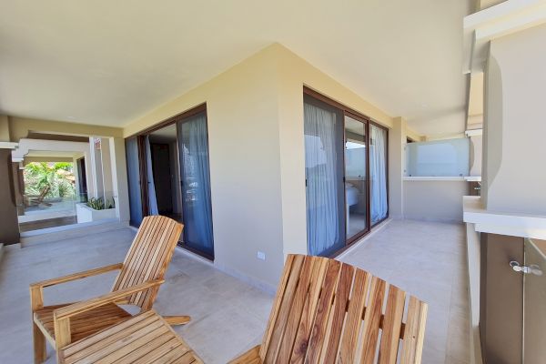 The image shows a patio area with wooden chairs, large sliding glass doors, and light-colored walls, giving a clean, modern, and open appearance.