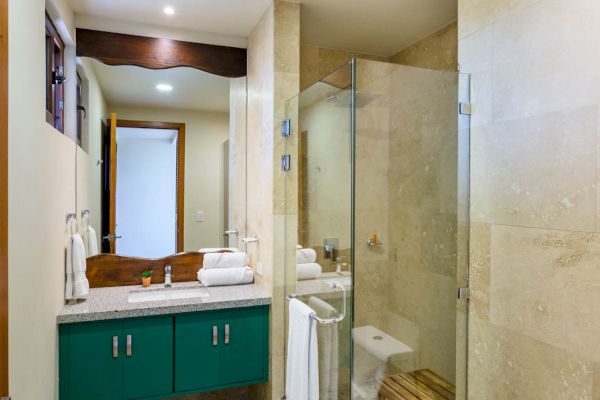 A bathroom with a glass-enclosed shower, a white toilet, a vanity with a sink, a mirror, and a towel. There is also a small stool in the shower.