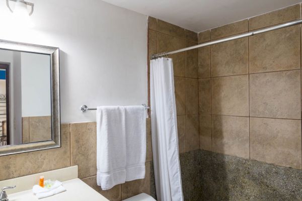 The image shows a bathroom with a sink, mirror, toilet, towel rack, and a shower area with tiles and a curtain.
