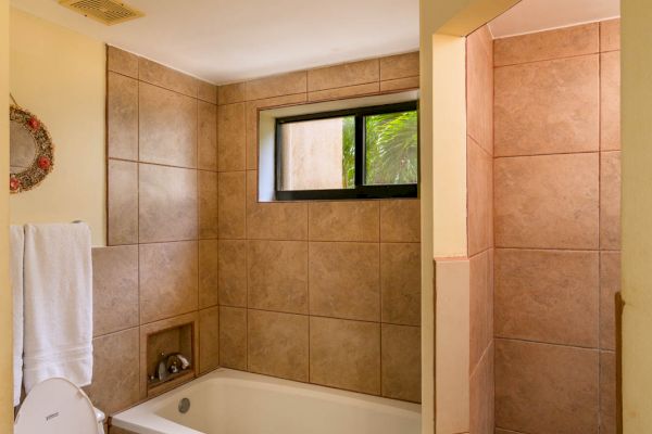 A bathroom with a toilet, bathtub, window, towel, and a walk-in shower with beige tiles and yellow walls is shown.