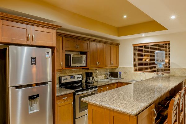 A modern kitchen with wooden cabinets, stainless steel appliances, a granite countertop, and a water dispenser on the counter.