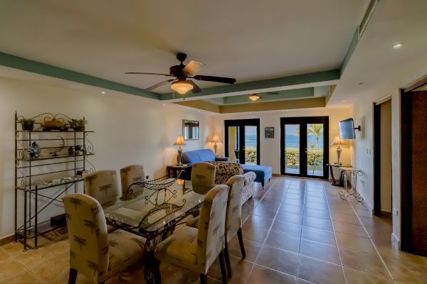 A well-furnished, cozy living and dining area with ceiling fans, couches, a dining table, and large windows offering a view of a garden or landscape.
