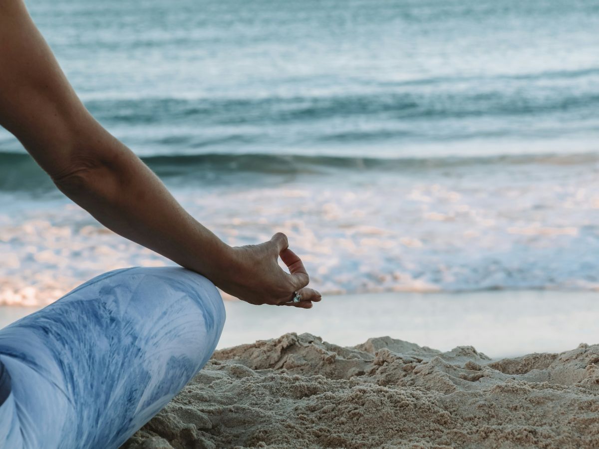 A person practicing yoga or meditation on a sandy beach, with the ocean waves gently crashing in the background.